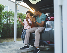 A father and son clap their hands while sitting together in the open trunk of an SUV.